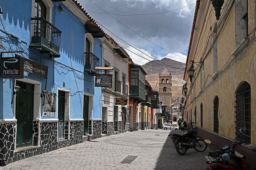 Calle colonial de Potosí con balcones de madera y, al fondo, la torre de una iglesia y la silueta del Cerro Rico.