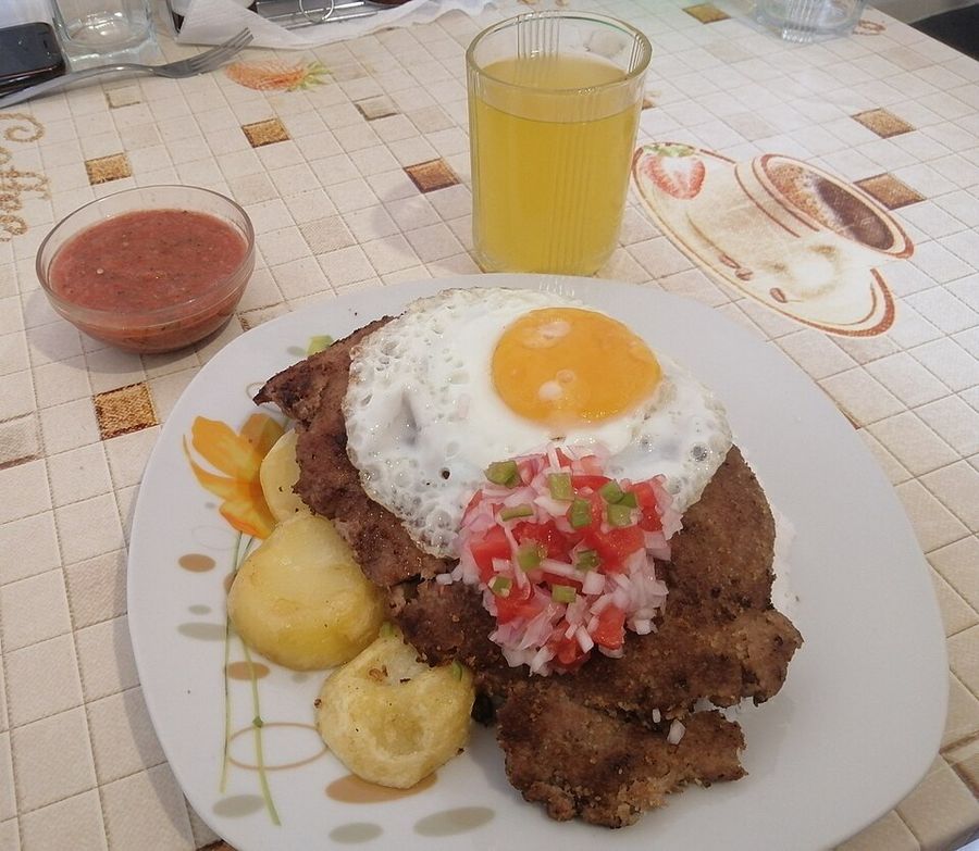 Plato de silpancho: una milanesa fina de carne apanada sobre arroz y papa, con un huevo frito encima y salsa criolla de tomate y cebolla.
